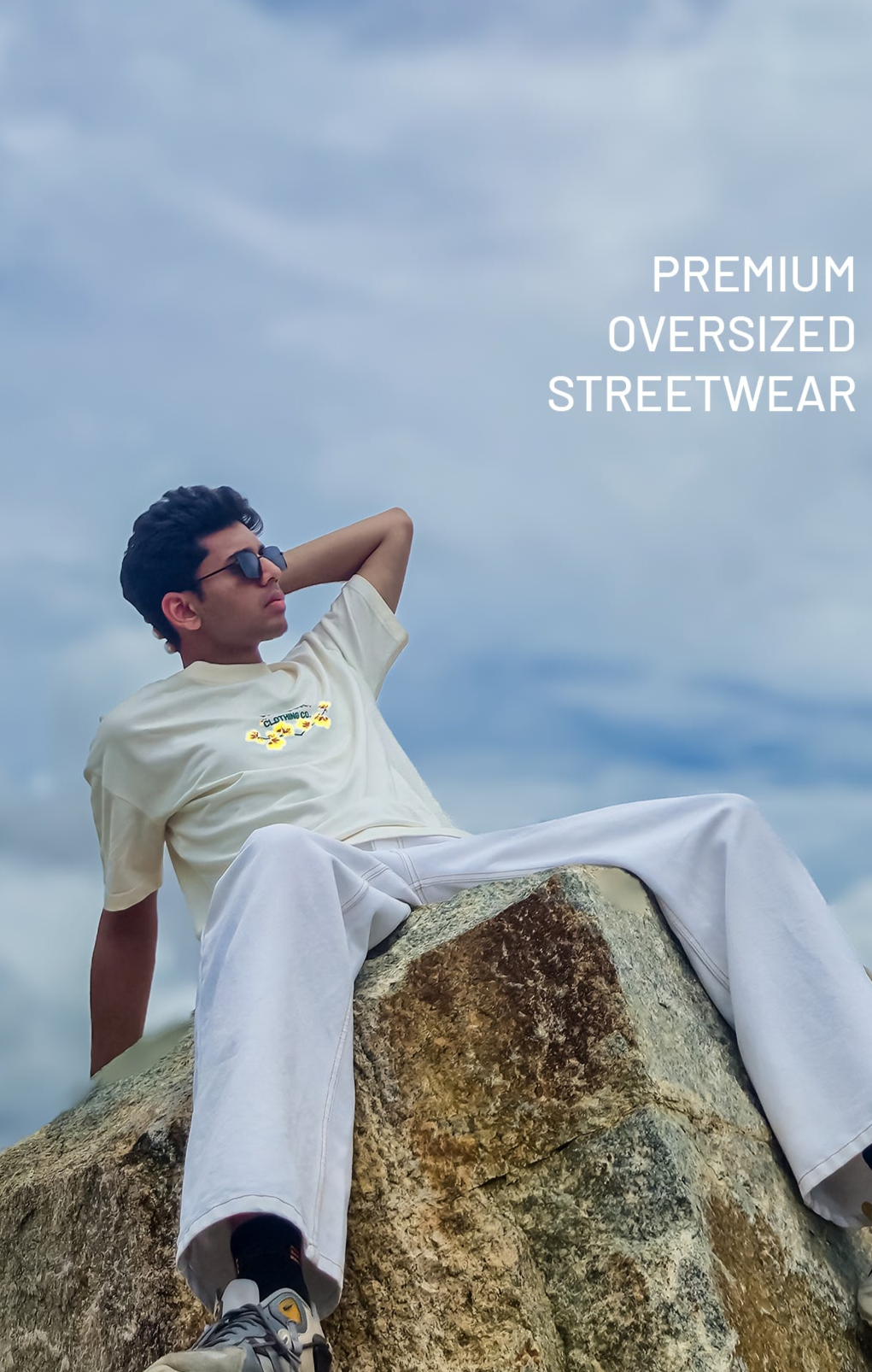 male model wearing a cream oversized t-shirt with Valour Clothing Co. logo, sitting outdoors; representing premium streetwear and luxury fit hero banner
