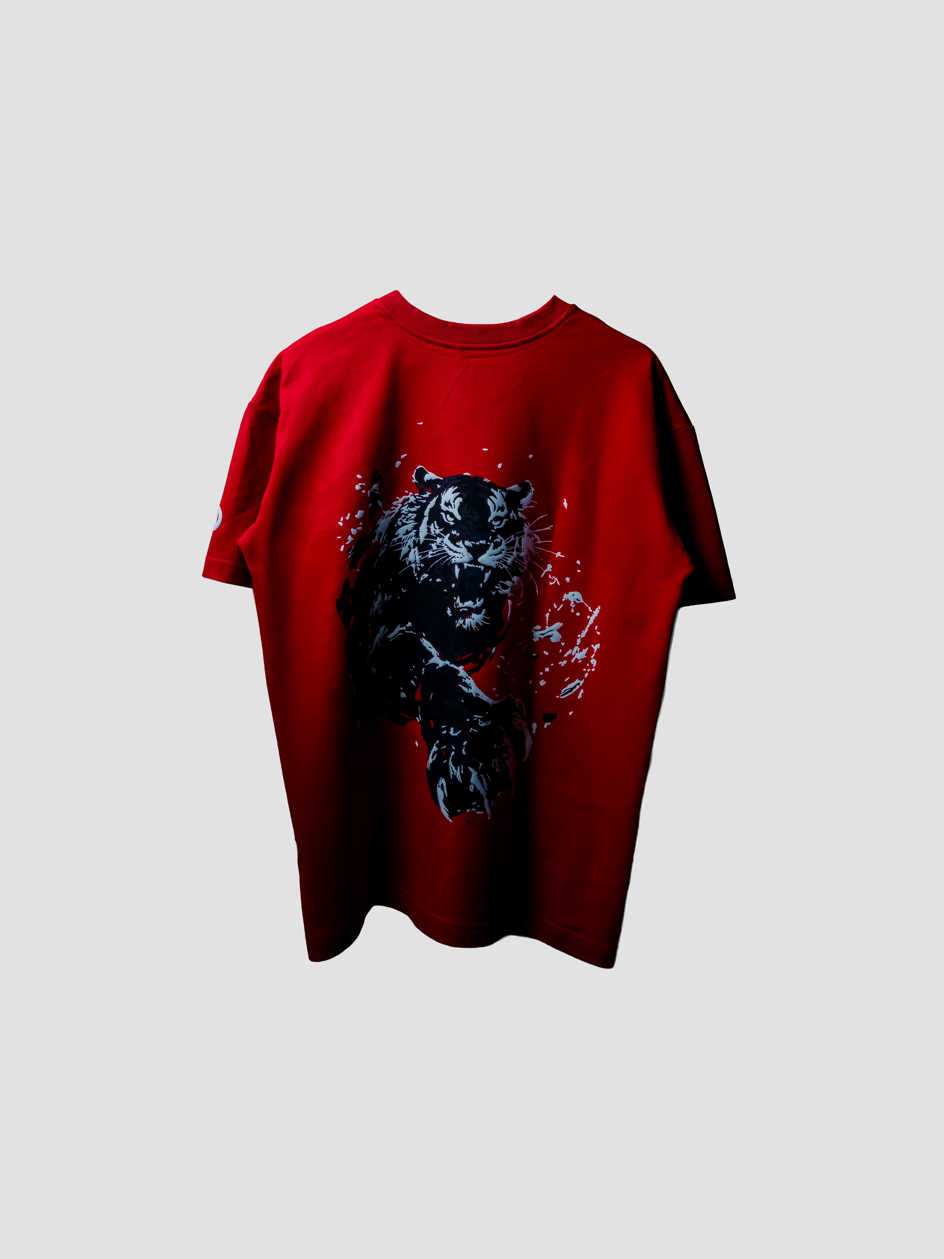 A red short-sleeve t-shirt featuring a large black tiger graphic on the back, set against a solid light gray background.