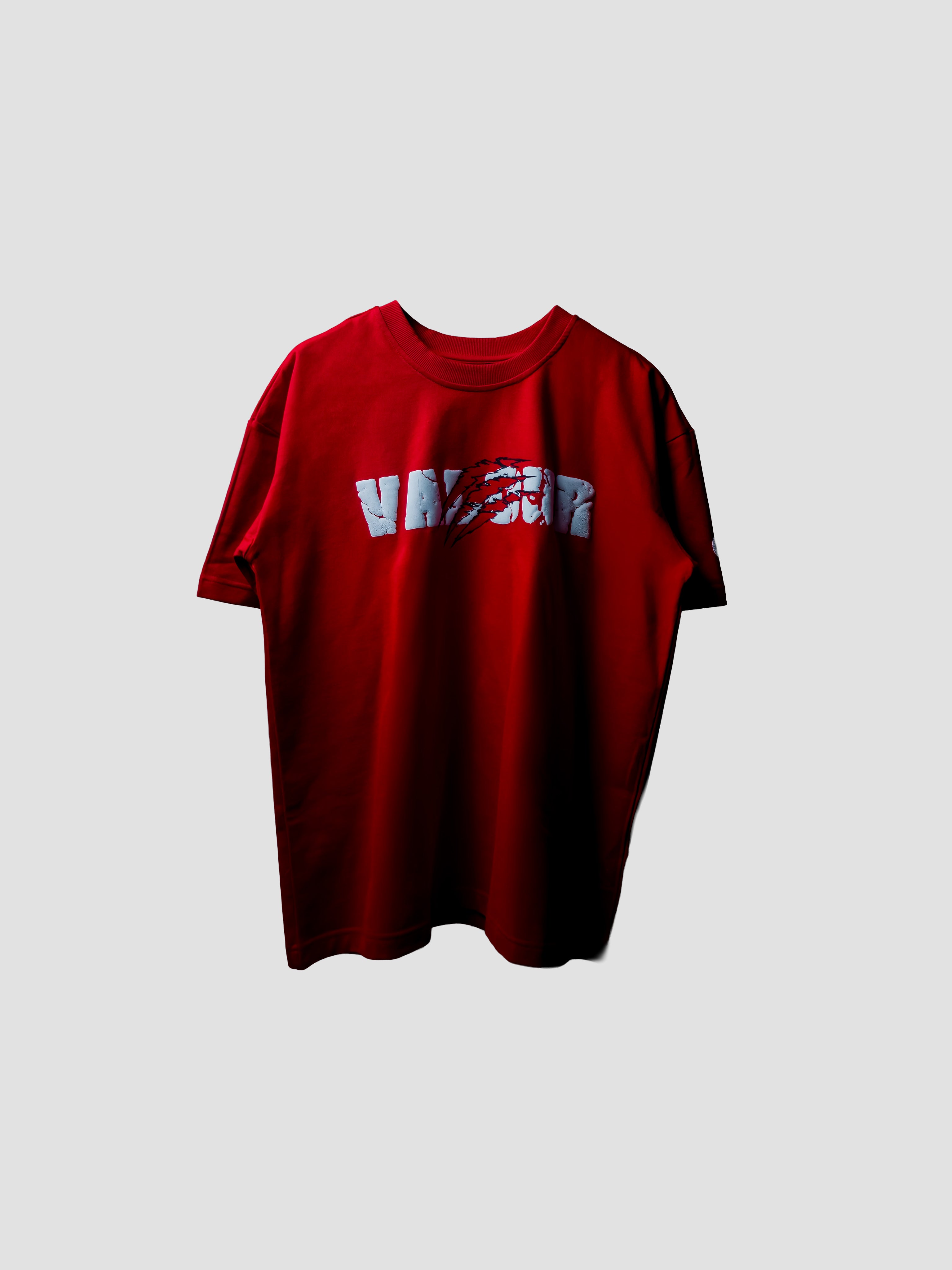 A red short-sleeve t-shirt with a distressed white graphic text print across the chest, displayed against a solid light gray background.