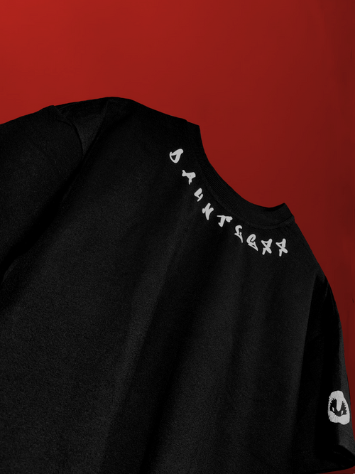 close-up detail of black oversized t-shirt neckline featuring white arched "DAUNTLESS" typography and subtle woven fabric texture