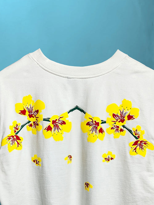 close-up detail of vibrant yellow and red floral print graphic near the neckline of a white oversized cotton t-shirt