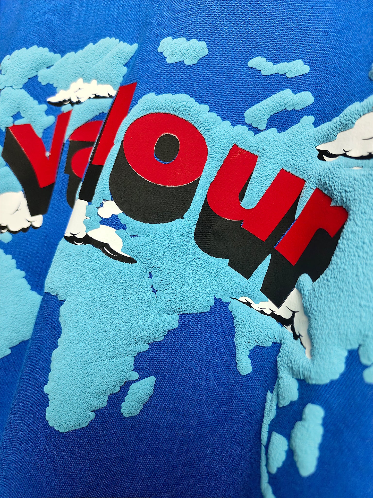 extreme close-up detail of 3D puff print world map graphic and layered red Valour text on blue oversized t-shirt texture