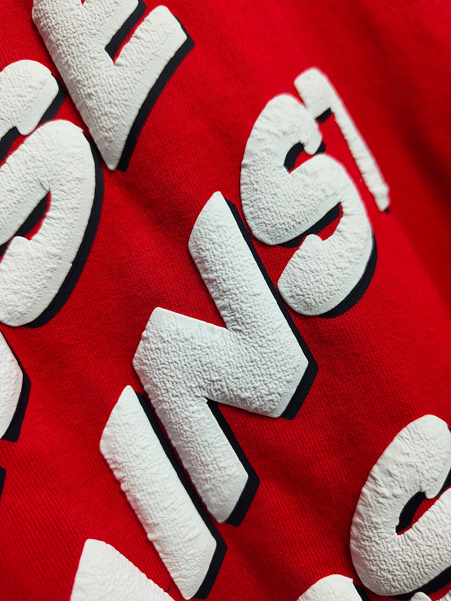 extreme close-up detail of white 3D puff print lettering texture on a vibrant red oversized cotton t-shirt
