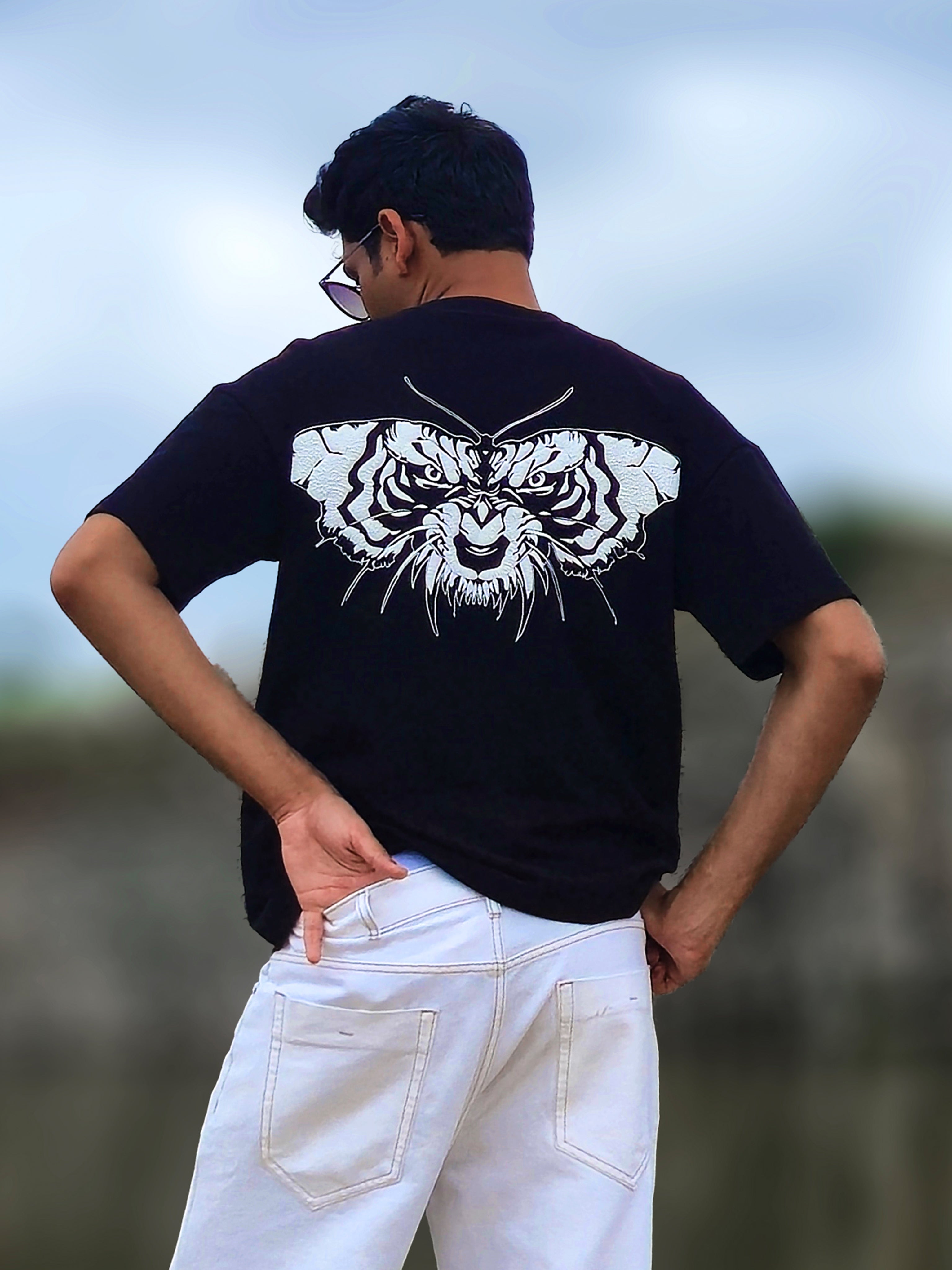 male model from behind wearing a black oversized t-shirt with a large white tiger face and butterfly wing graphic on the back