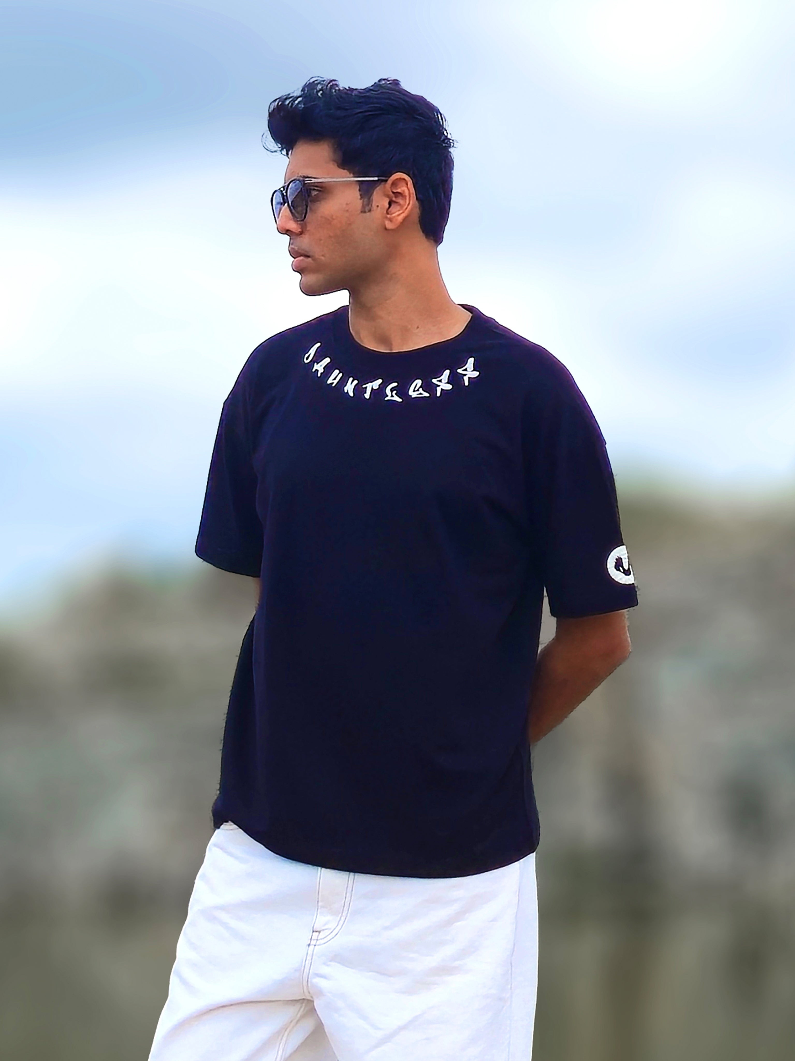 male model wearing a black oversized t-shirt with white "DAUNTLESS" neckline typography and a small sleeve logo, styled with white pants