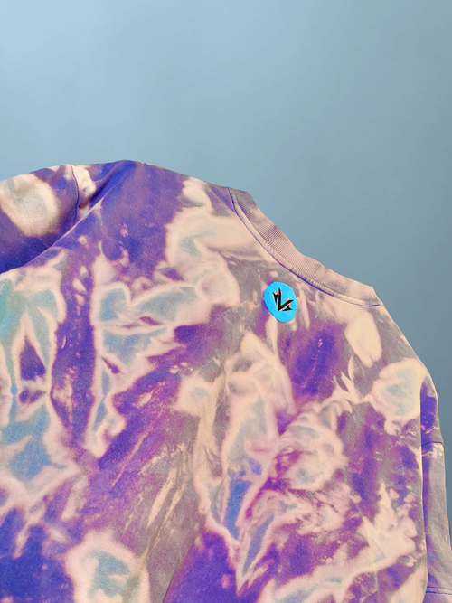 close-up detail of purple and blue acid wash oversized t-shirt texture featuring a small round neon blue chest logo with the Valour letter V